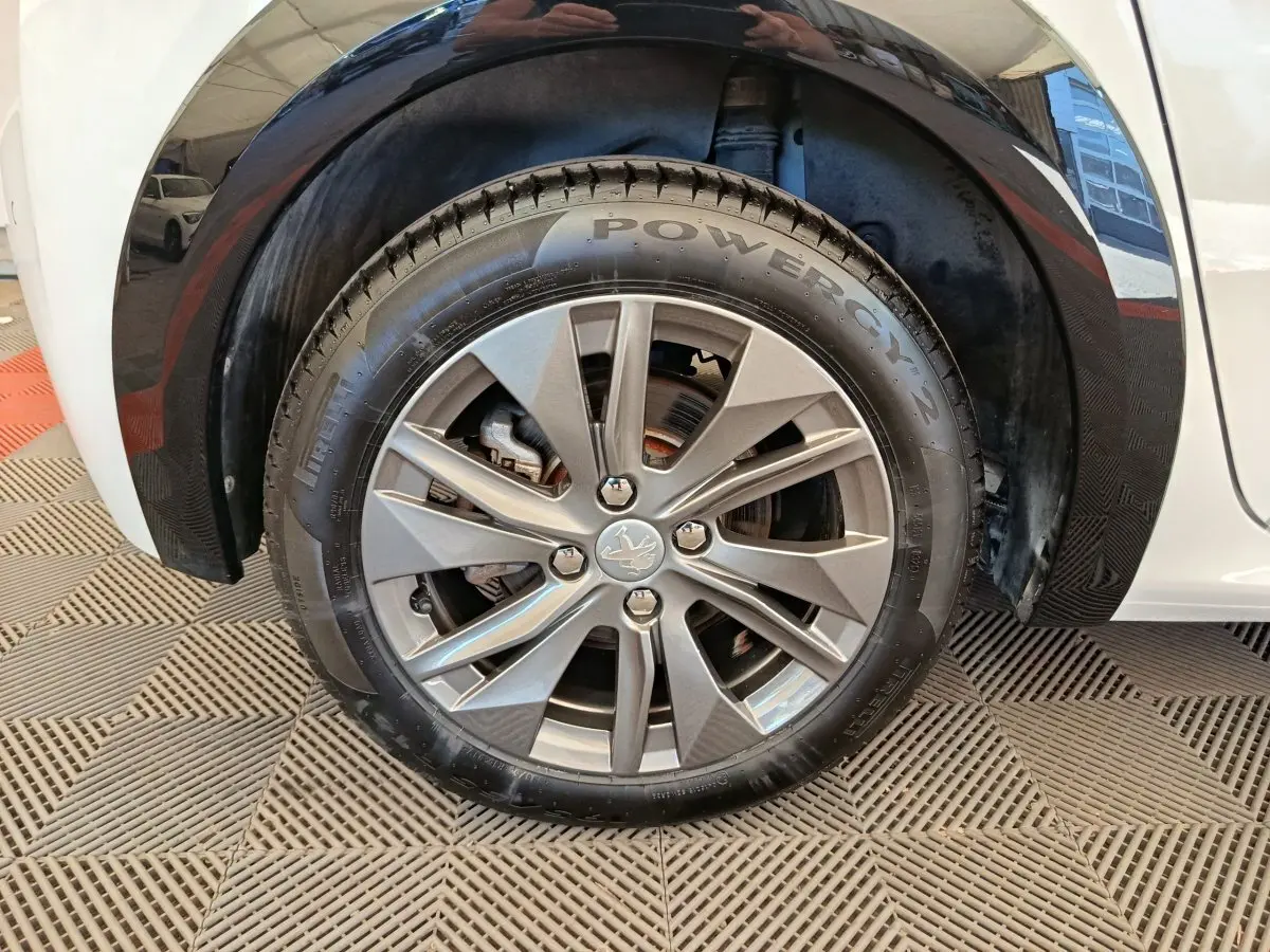 Gros plan sur la roue avant droite d'une Peugeot 208 électrique blanche, avec jante alliage et logo lion central.