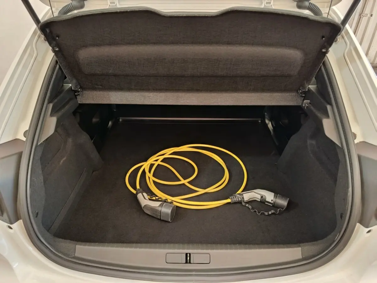 Coffre ouvert d’une Peugeot 208 électrique blanche, vue arrière, avec câble de recharge jaune visible à l’intérieur.