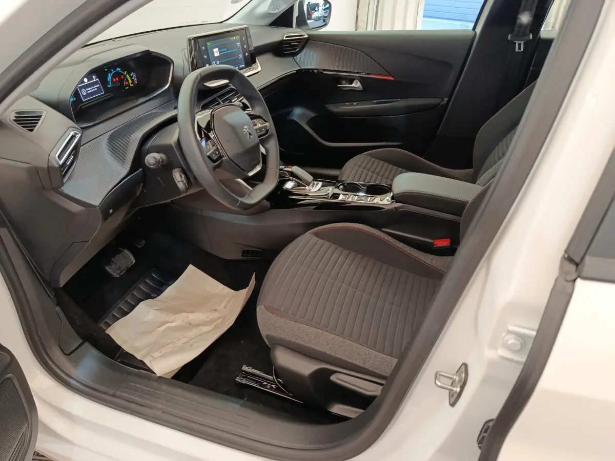 Intérieur côté conducteur de la Peugeot 208 électrique blanche, avec tableau de bord numérique et volant compact multifonctions.