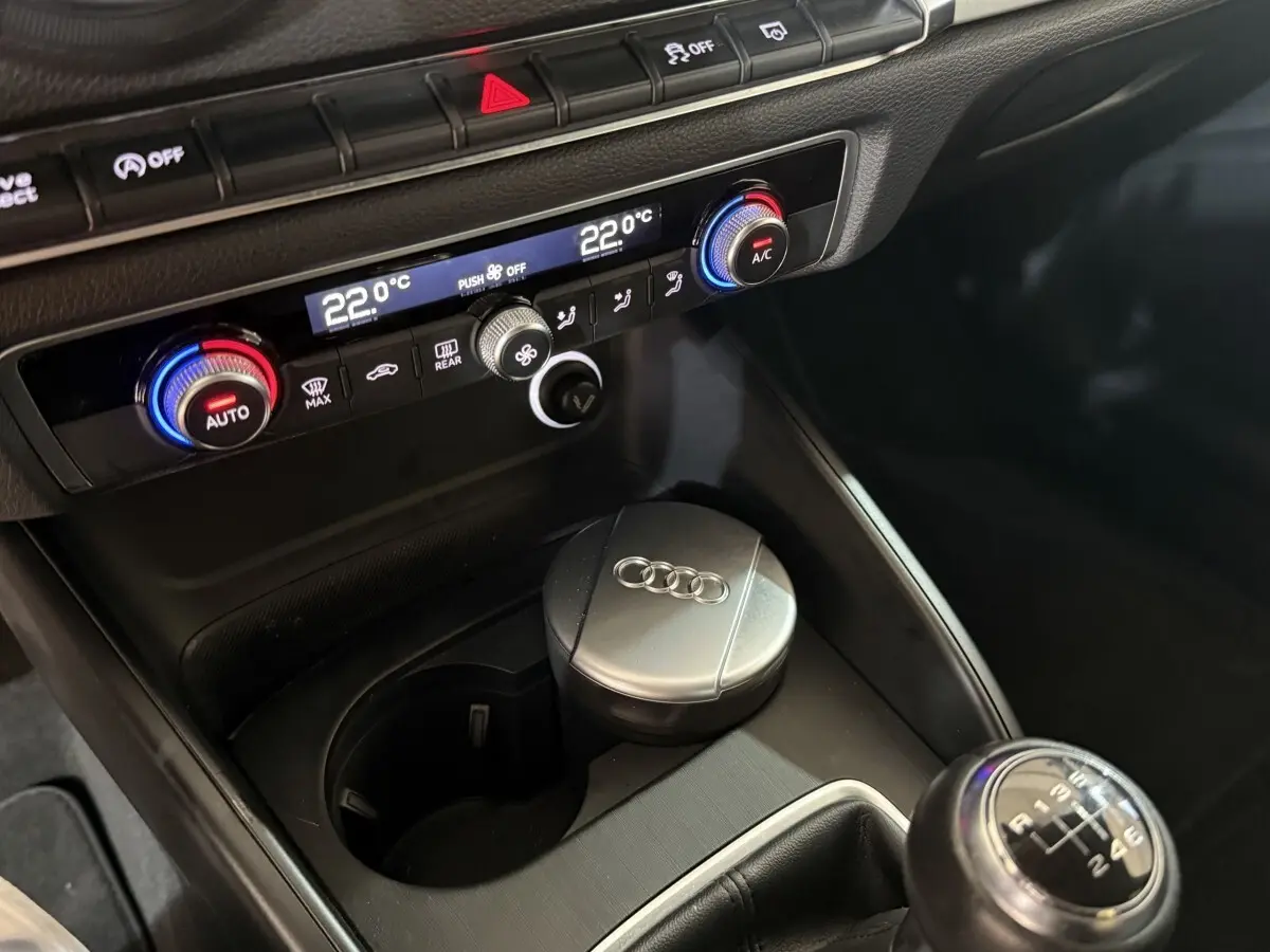 Gros plan sur la console centrale de l'Audi A3 bleu 2018, montrant la climatisation digitale et le levier de vitesses manuel.