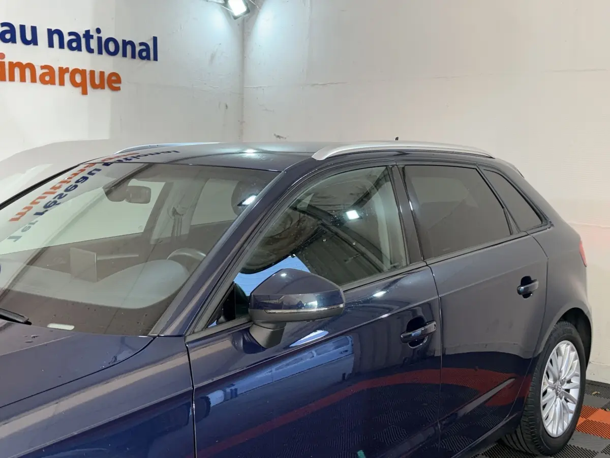 Vue de profil côté gauche d'une Audi A3 bleu foncé 2018 avec rétroviseur et jantes visibles dans un showroom.