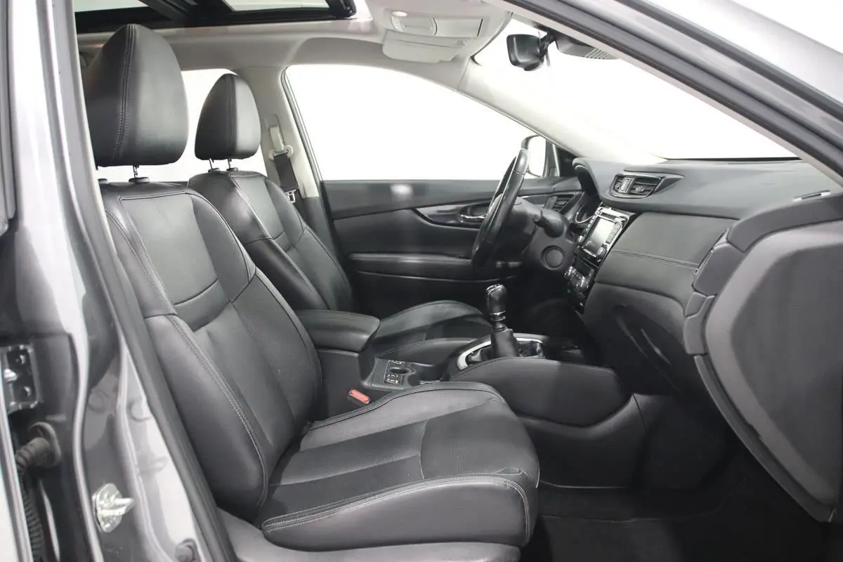 Vue intérieure côté conducteur du Nissan X-TRAIL gris métallisé 2021, sièges cuir noirs et boîte manuelle visible.