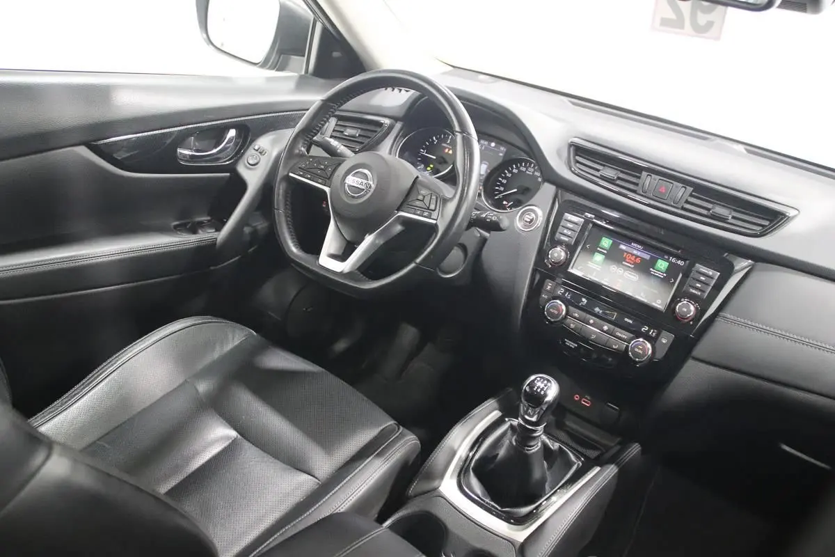 Vue intérieure côté conducteur du Nissan X-TRAIL 1.7 D 150 avec volant cuir, sièges noirs et boîte manuelle.