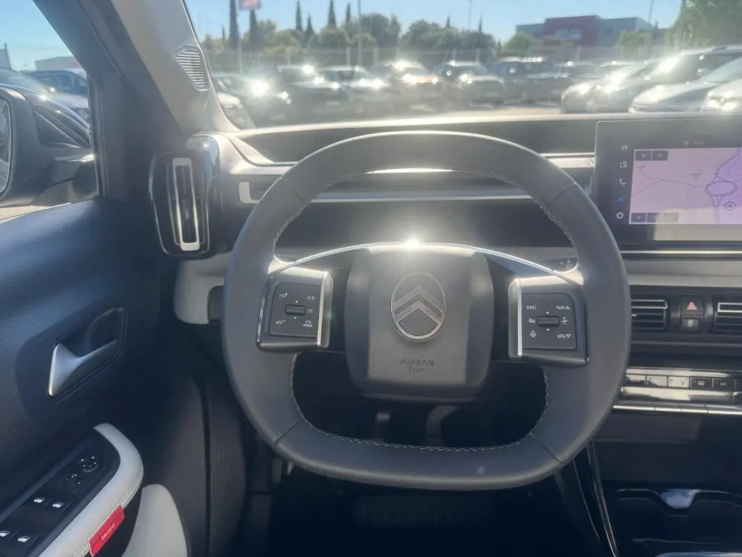 Vue intérieure centrée sur le volant de la Citroën C3 gris 2025, avec commandes intégrées et écran tactile visible.