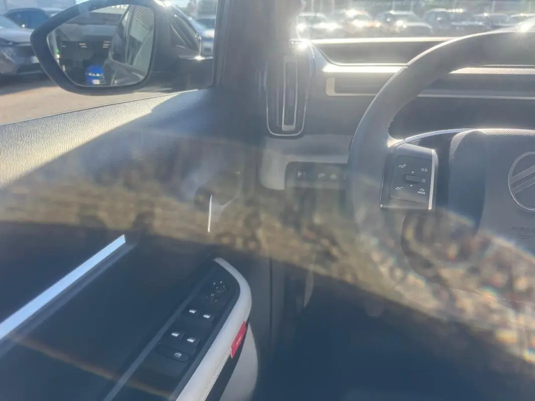 Vue intérieure côté conducteur de la Citroën C3 gris 2025, avec commandes des vitres et rétroviseur électrique visibles.