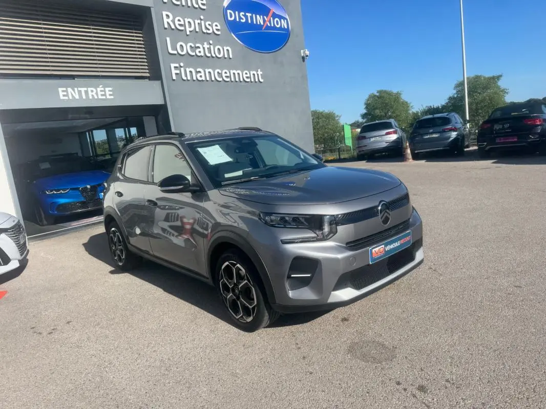 Citroën C3 gris 3/4 avant droit avec barres de toit et jantes alliage 17 pouces, stationnée devant un concessionnaire.