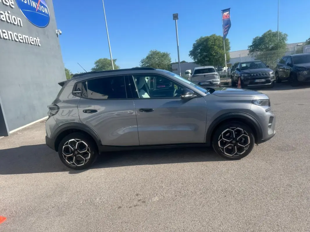 Vue de profil côté gauche d'une Citroën C3 gris métallisé 2025 avec jantes alliage 17 pouces et barres de toit noires.