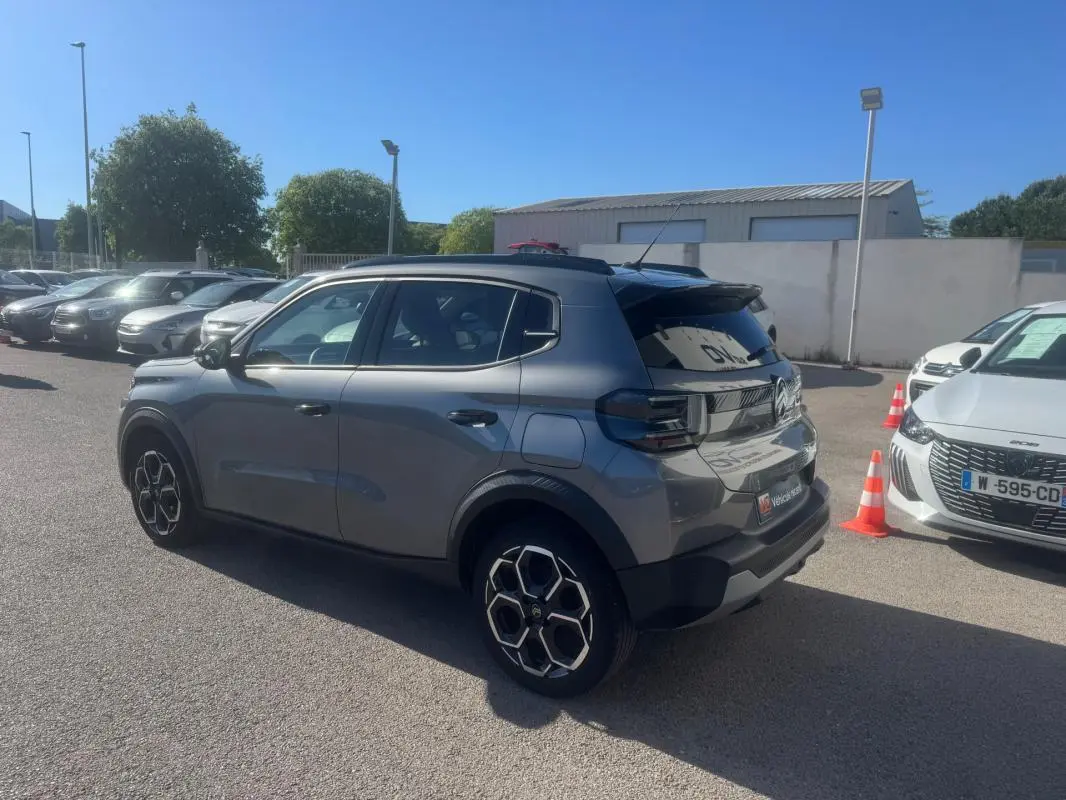 Vue 3/4 arrière droite d'une Citroën C3 gris 2025 avec jantes alliage 17 pouces et barres de toit noires.