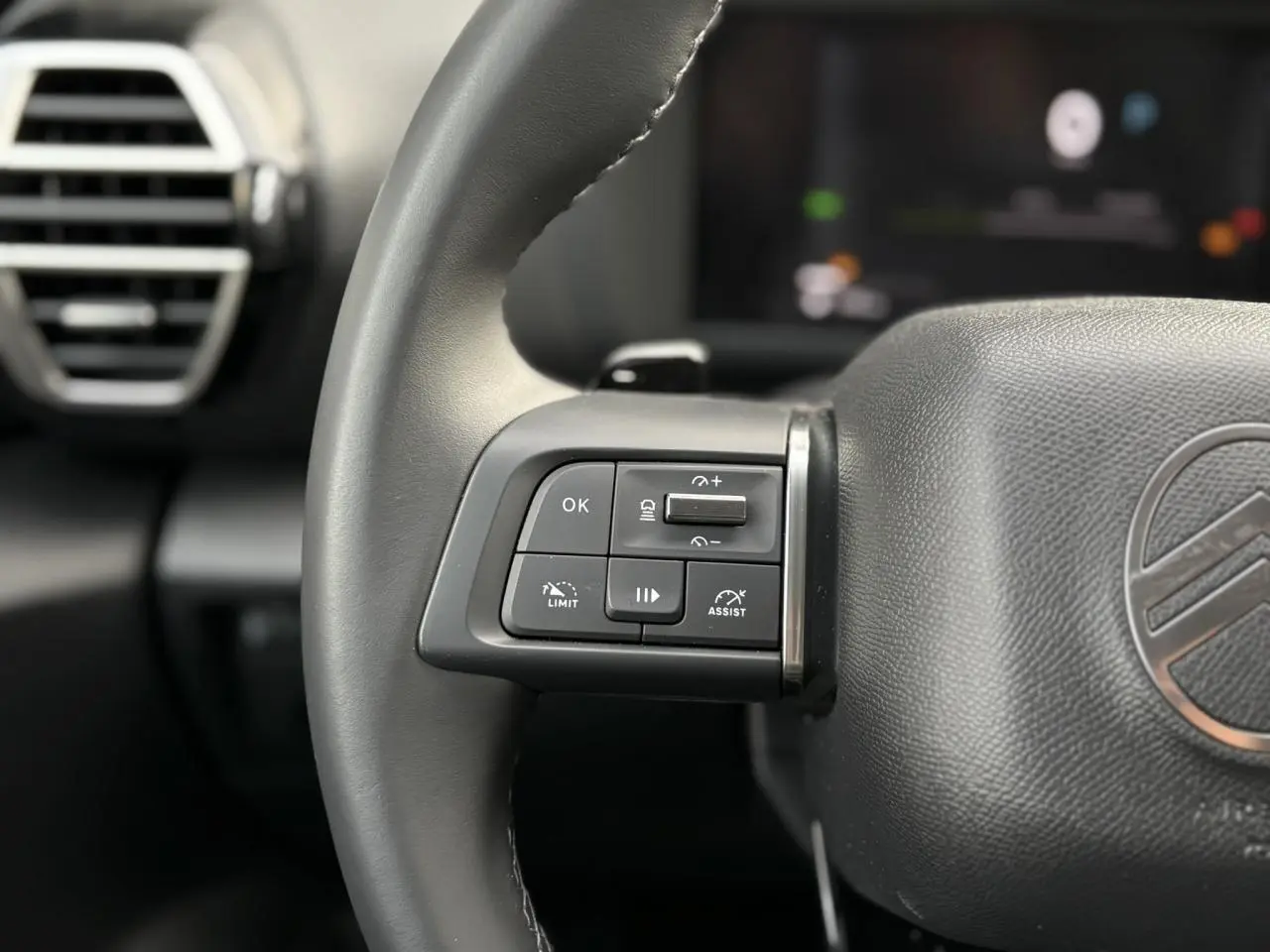 Gros plan sur les commandes au volant côté gauche en cuir noir du Citroën C4 Hybrid gris Mercury, avec aérateur en arrière-plan.