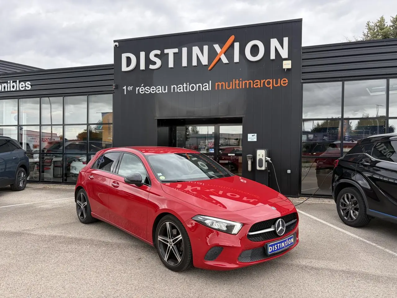 Vue 3/4 avant d'une Mercedes Classe A rouge avec jantes alliage noires, garée devant un bâtiment Distinxion.