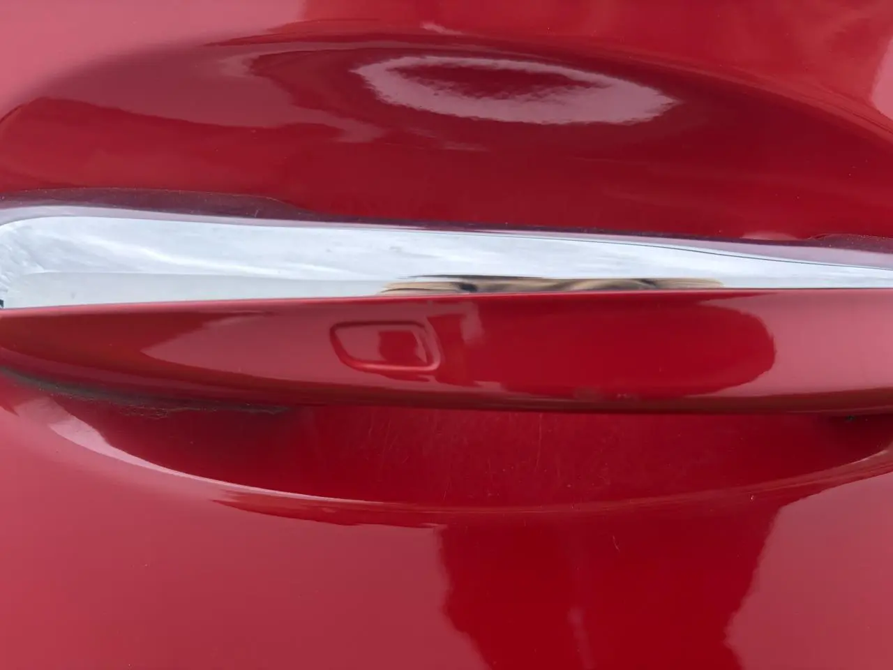 Gros plan sur la poignée de porte chromée d'une Mercedes Classe A rouge, finition Progressive Line.
