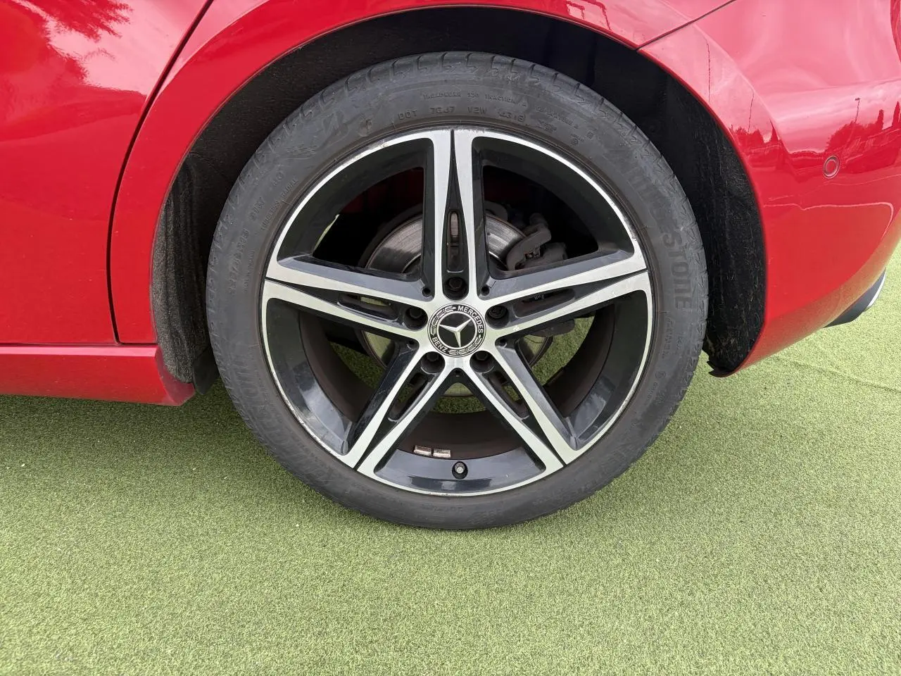 Gros plan sur la roue arrière droite d'une Mercedes Classe A rouge avec jante alliage 5 branches noir et argent.