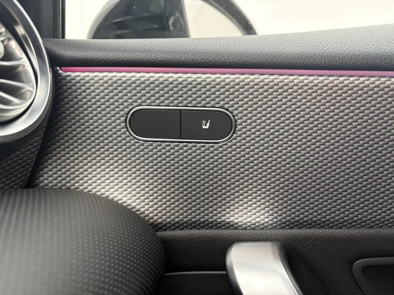 Gros plan sur la commande de siège chauffant intégrée dans la garniture effet carbone à l'intérieur d'une Mercedes Classe A rouge.