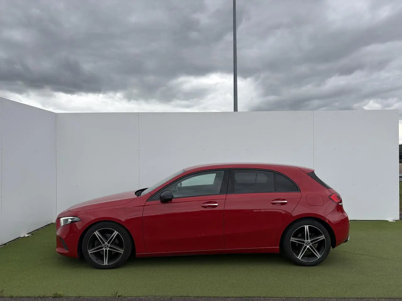 Vue latérale droite d'une Mercedes Classe A rouge avec jantes alliage noires à 5 branches, sur fond neutre extérieur.