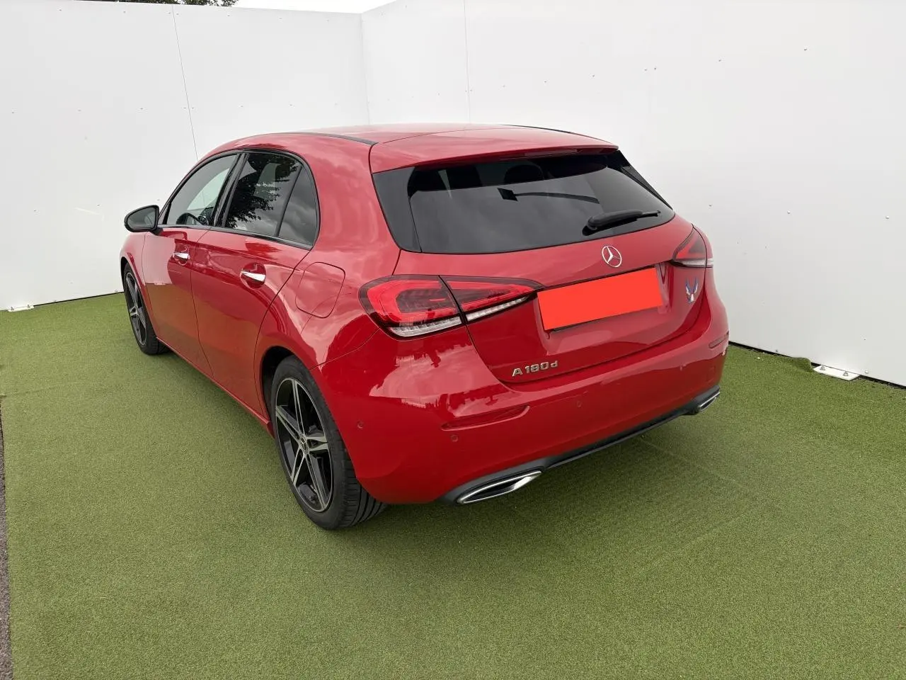Vue 3/4 arrière gauche d'une Mercedes Classe A 180d rouge avec vitres teintées et jantes alliage noires à 5 branches.