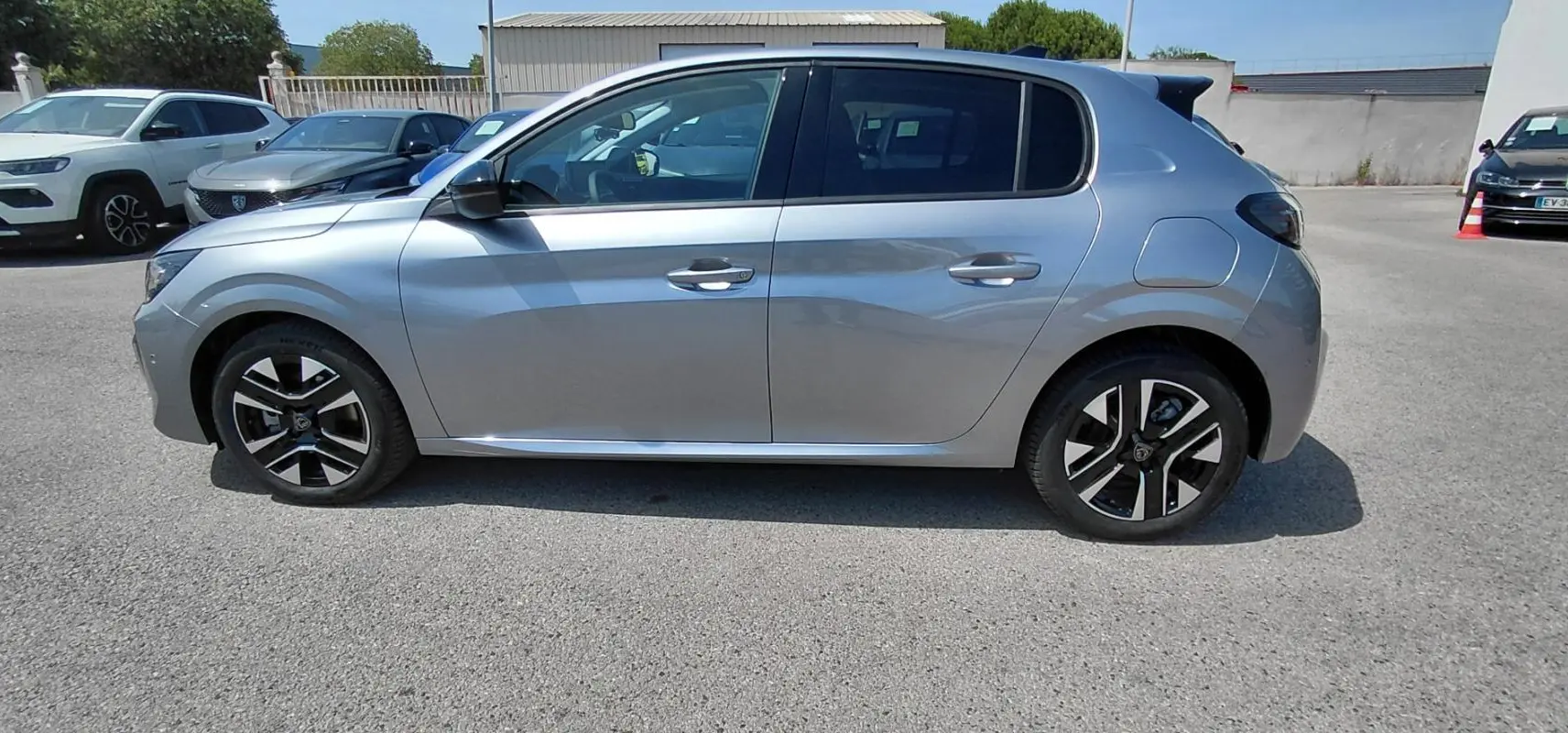 Peugeot 208 Hybrid gris vue de profil côté gauche, avec jantes alliage noires et argentées visibles.