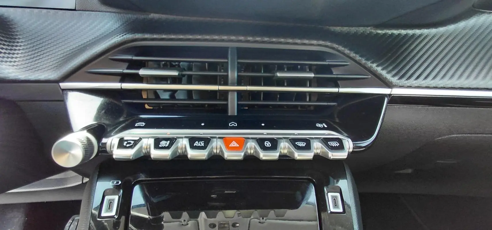 Gros plan sur la console centrale du Peugeot 208 gris 2025, avec boutons de commande et aérateurs noirs.