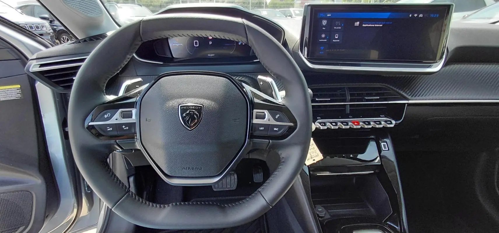 Vue intérieure centrée sur le volant cuir noir et le cockpit numérique de la Peugeot 208 gris 2025 Hybrid Allure.