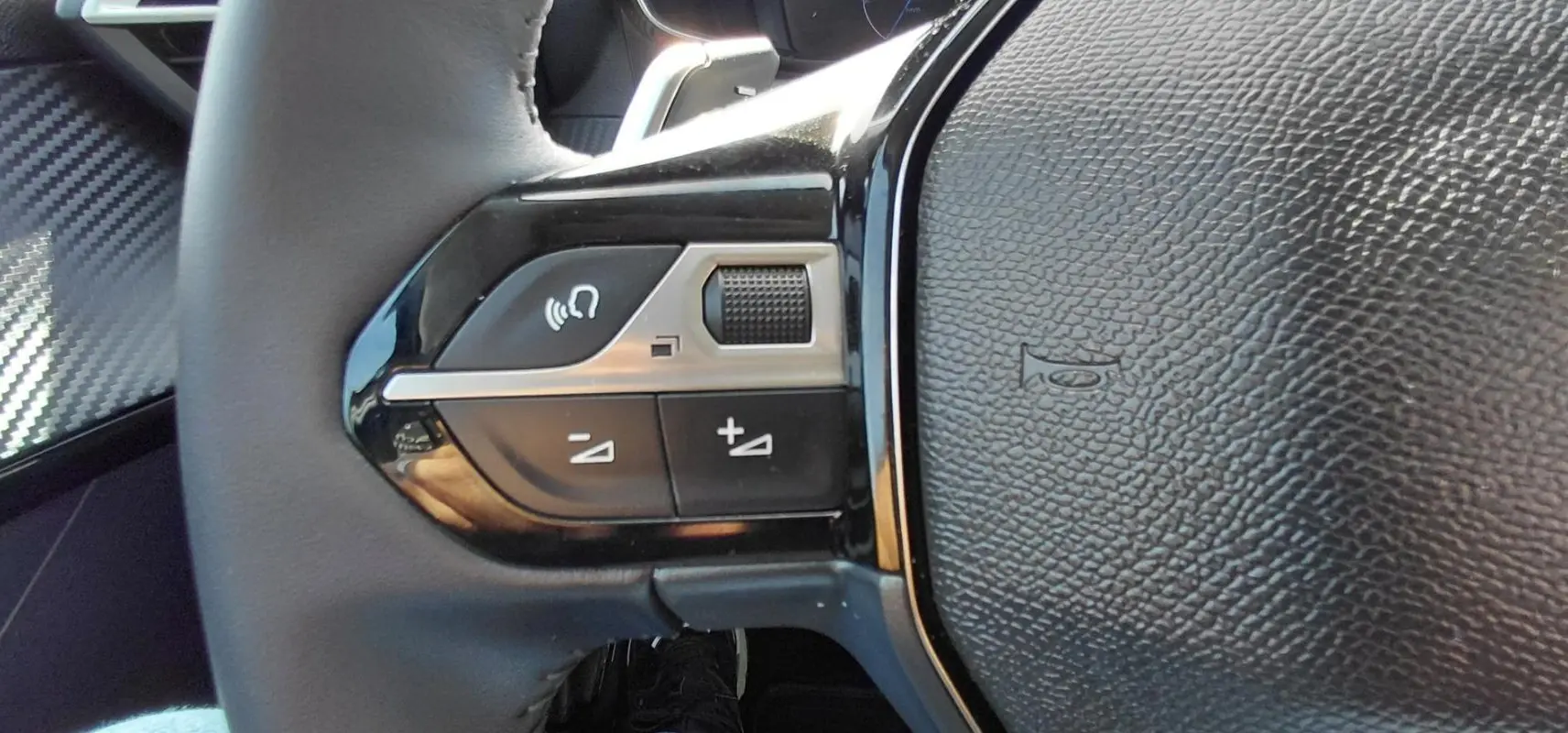Gros plan sur les commandes gauche du volant en cuir noir du Peugeot 208 gris, avec boutons de volume et fonction mains libres.
