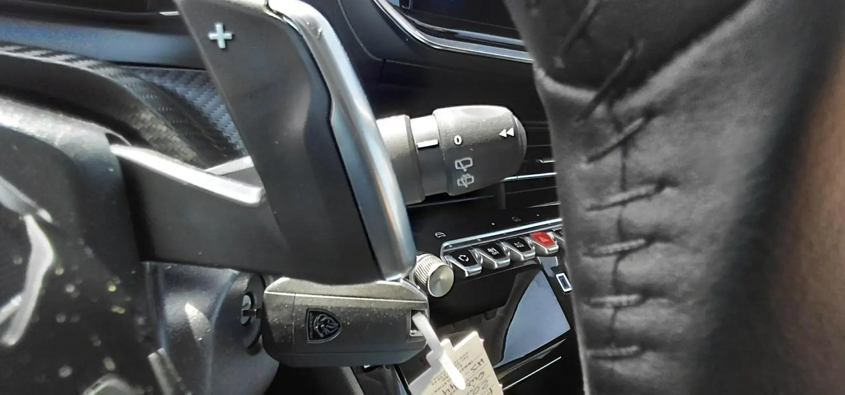 Gros plan sur le volant et la commande de clignotant d’une Peugeot 208 Hybrid gris, avec détails des boutons du tableau de bord.