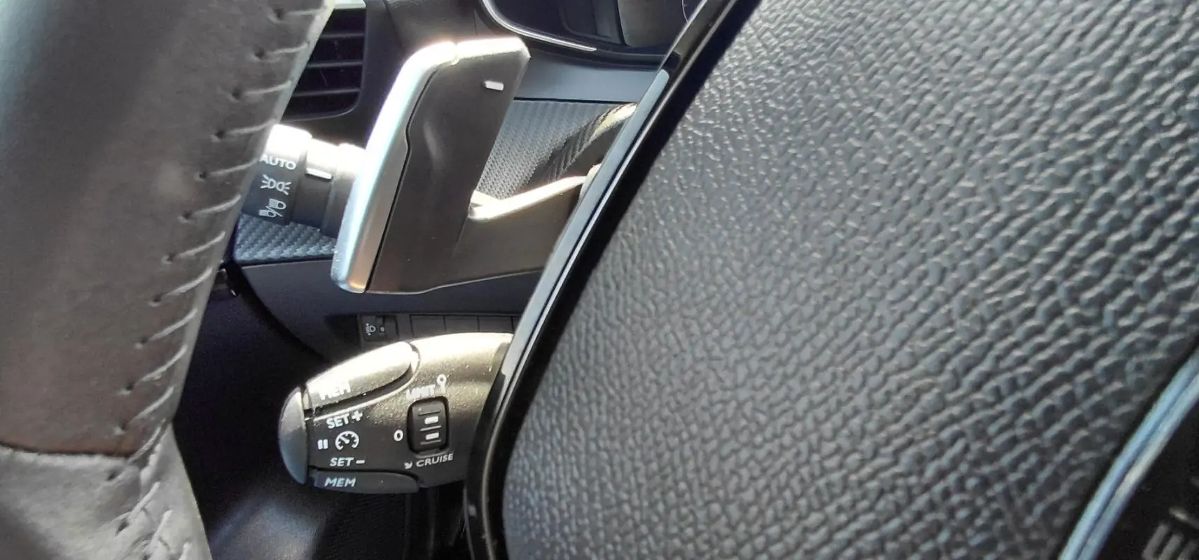 Gros plan sur le volant et la commande de régulateur de vitesse d’une Peugeot 208 gris, intérieur moderne et texturé.