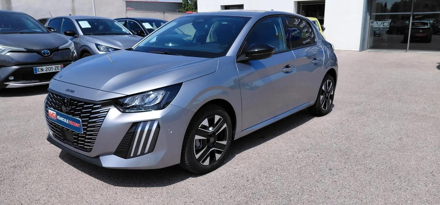 Peugeot 208 Hybrid gris vue 3/4 avant droit, avec calandre distinctive et jantes alliage 16 pouces.