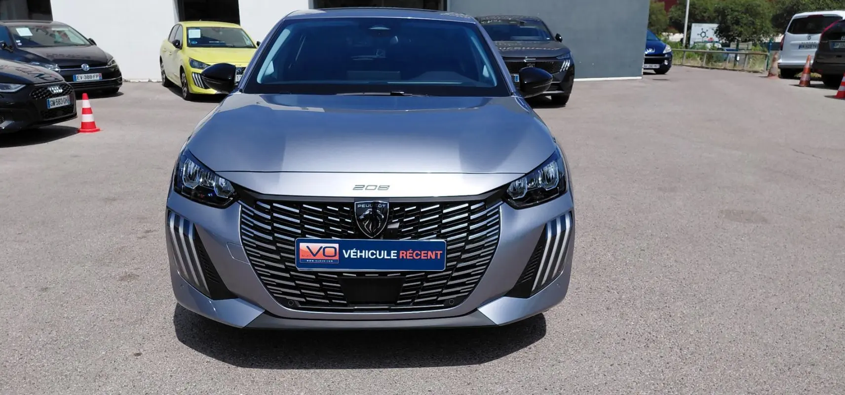 Vue avant d'une Peugeot 208 gris métallisé 2025 avec calandre noire distinctive et feux LED en forme de griffes.