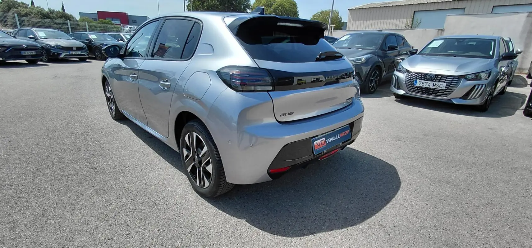 Vue 3/4 arrière gauche d'une Peugeot 208 gris clair avec jantes alliage et feux arrière noirs, stationnée en extérieur.