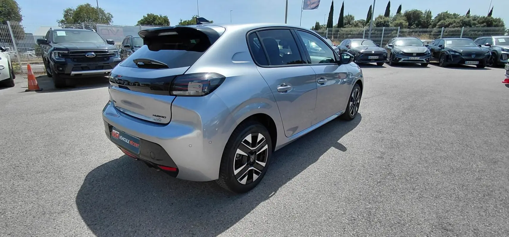 Vue 3/4 arrière droit d'une Peugeot 208 Hybrid gris métallisé avec jantes alliage et feux arrière fumés.