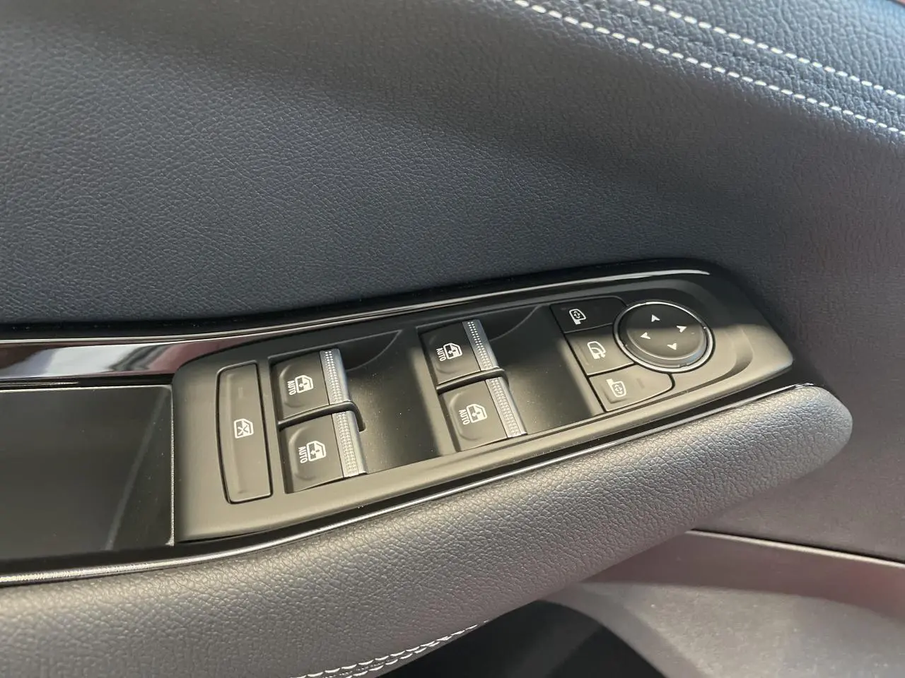 Gros plan sur les commandes de lève-vitres et rétroviseurs sur la porte côté conducteur en finition textile gris foncé.