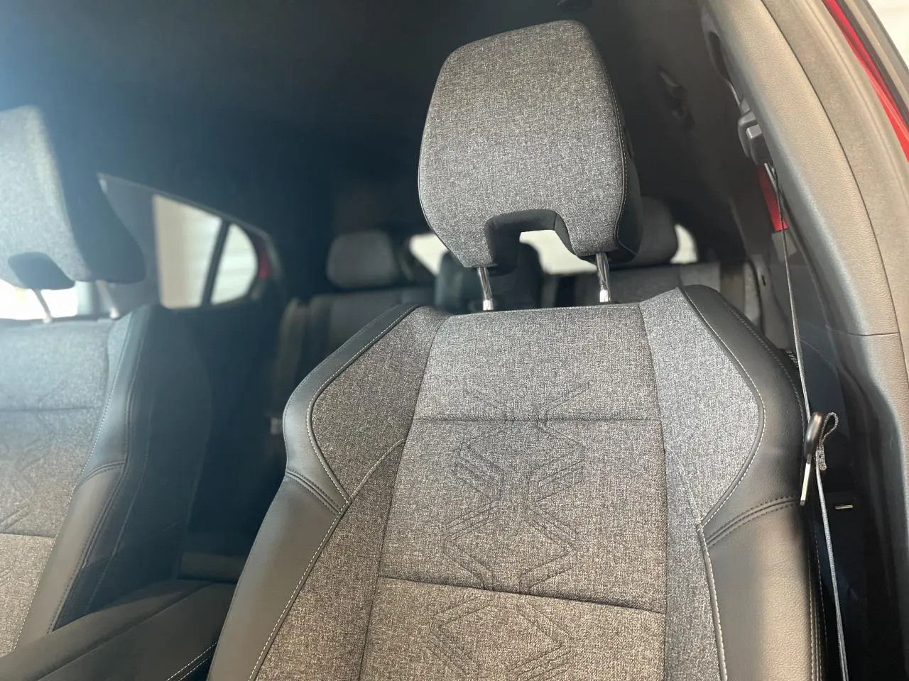 Gros plan sur le siège avant en textile gris et cuir noir du Renault Rafale rouge avec toit noir, intérieur visible en arrière-plan.