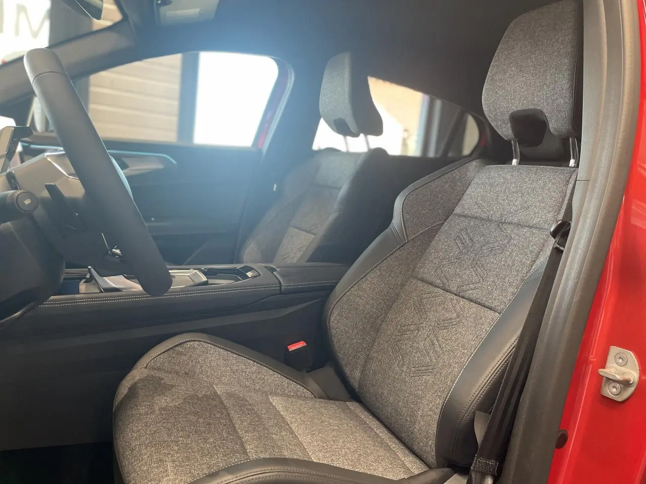 Intérieur côté conducteur du Renault Rafale 2025, siège sport gris textile avec surpiqûres, porte rouge visible.
