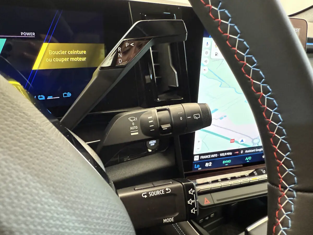 Détail intérieur côté conducteur du levier de vitesses et commandes sur volant cuir noir avec surpiqûres tricolores du Renault Espace hybride.