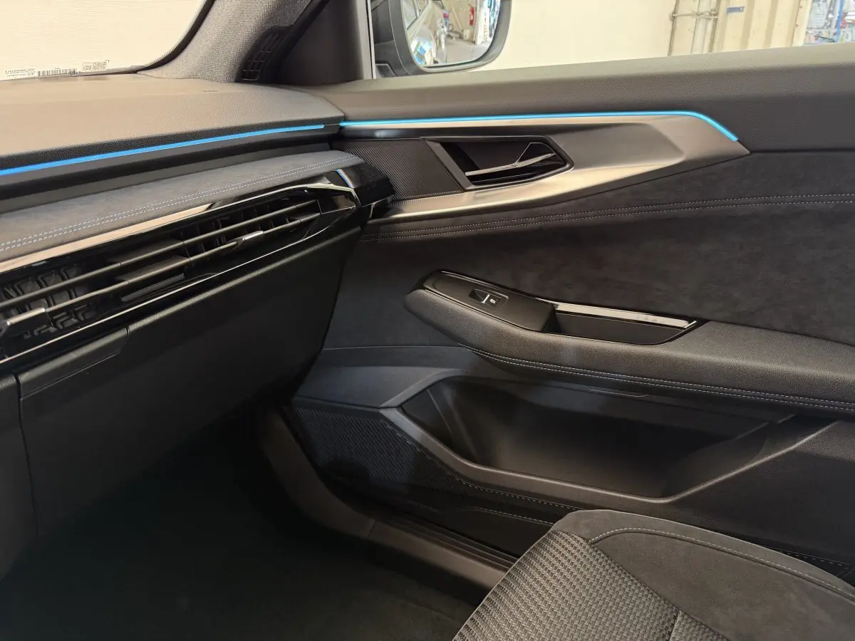 Intérieur côté passager du Renault Espace gris foncé 2025, avec éclairage d'ambiance bleu et garnitures noires élégantes.