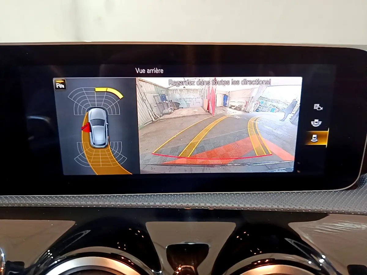 Écran tactile intérieur montrant la caméra de recul et l'aide au stationnement d'une Mercedes Classe A 180 AMG Line noire.