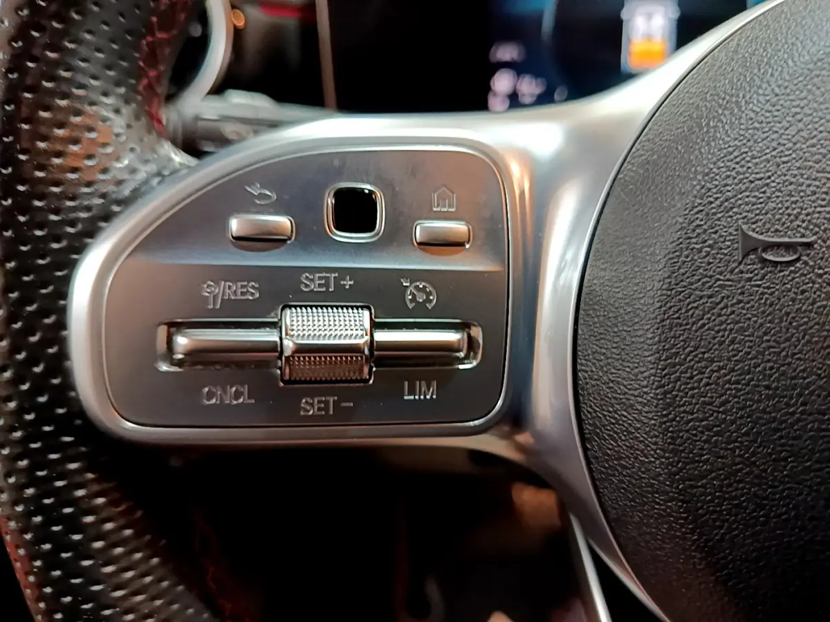 Gros plan sur les commandes du volant côté gauche en cuir perforé de la Mercedes Classe A 180 AMG Line noire.
