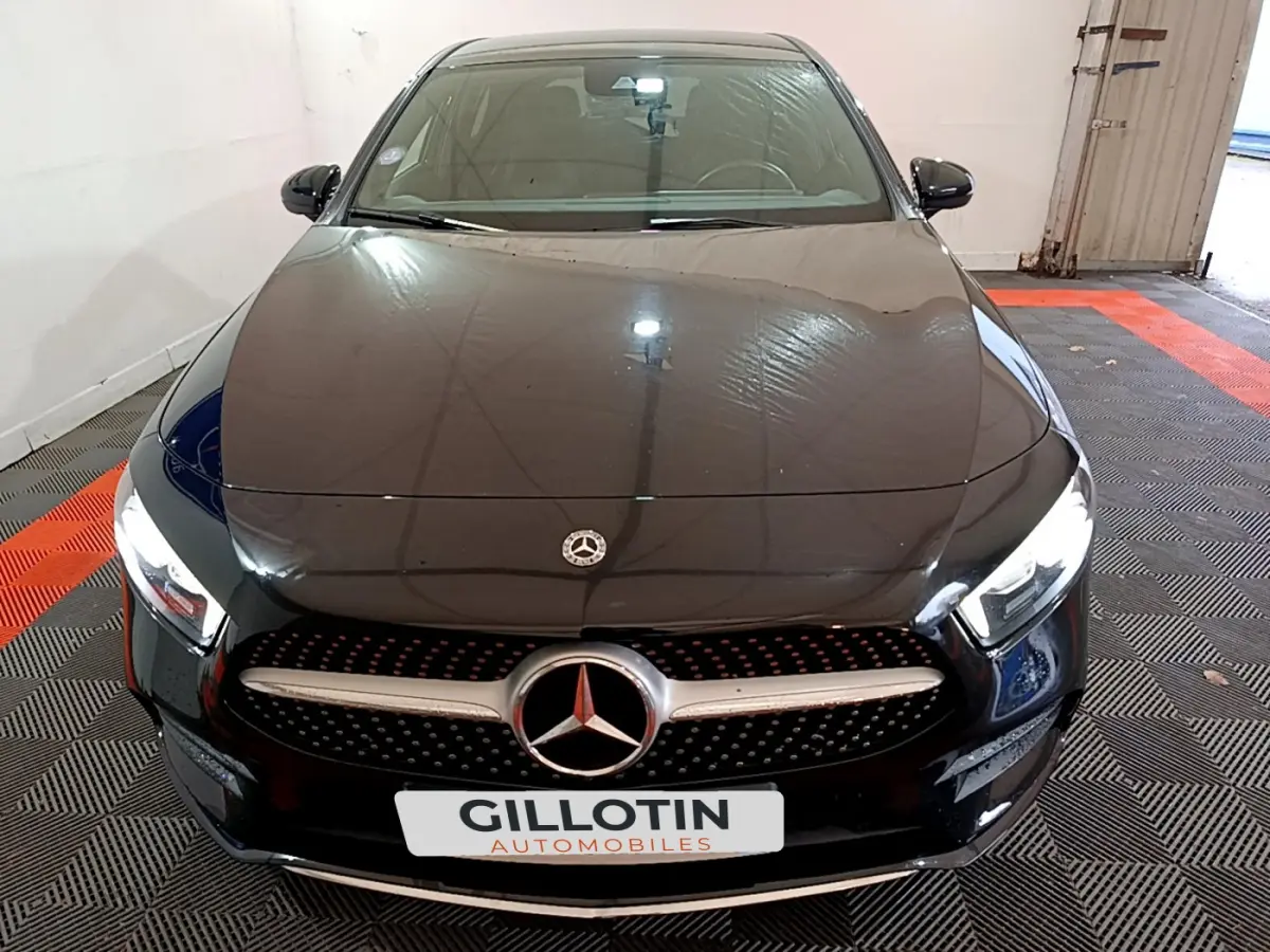Vue avant d'une Mercedes Classe A 180 AMG Line noire avec calandre étoilée et phares LED allumés.