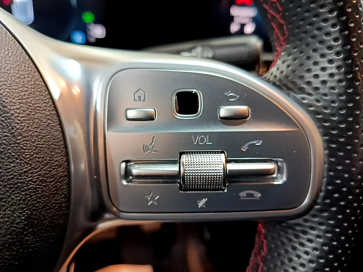 Gros plan sur les commandes de volume et téléphone au volant cuir perforé rouge d'une Mercedes Classe A 180 AMG Line noire.