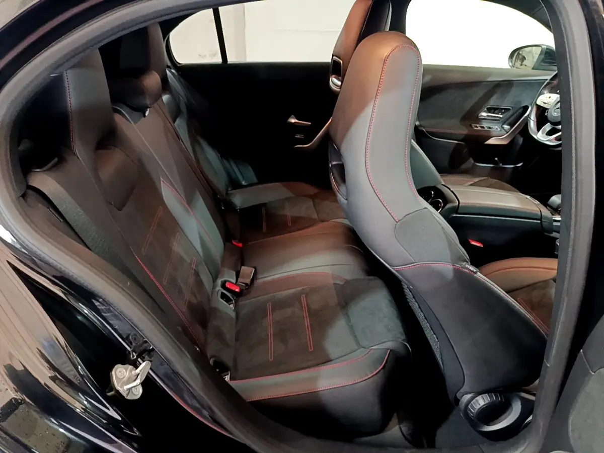 Vue intérieure côté gauche de la Mercedes Classe A 180 AMG Line noire, sièges sport noirs avec surpiqûres rouges.