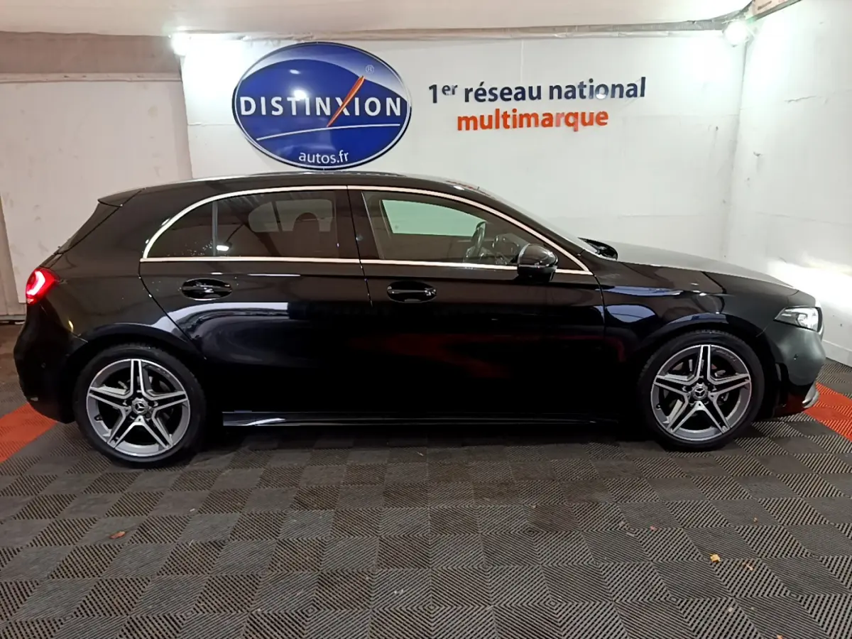Profil droit d'une Mercedes Classe A 180 AMG Line noire avec jantes alliage cinq branches en intérieur showroom.