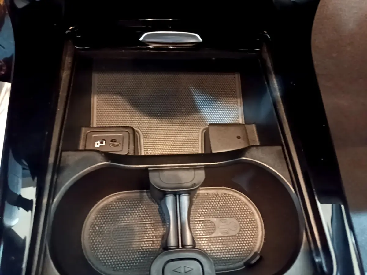 Gros plan sur la console centrale noire de la Mercedes Classe A 180 AMG Line, avec porte-gobelets et recharge sans fil.