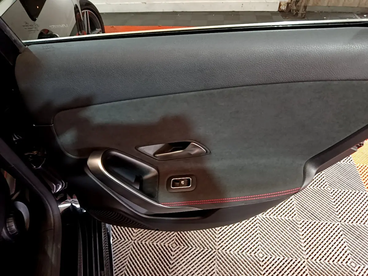 Gros plan sur la porte intérieure côté gauche d'une Mercedes Classe A 180 AMG Line noire avec surpiqûres rouges.