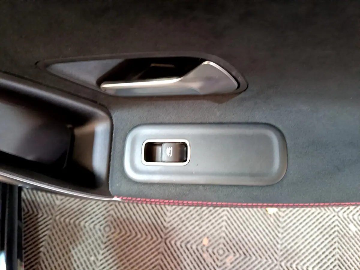 Gros plan sur la commande de lève-vitre côté gauche d'une Mercedes Classe A 180 AMG Line noire, avec surpiqûres rouges.