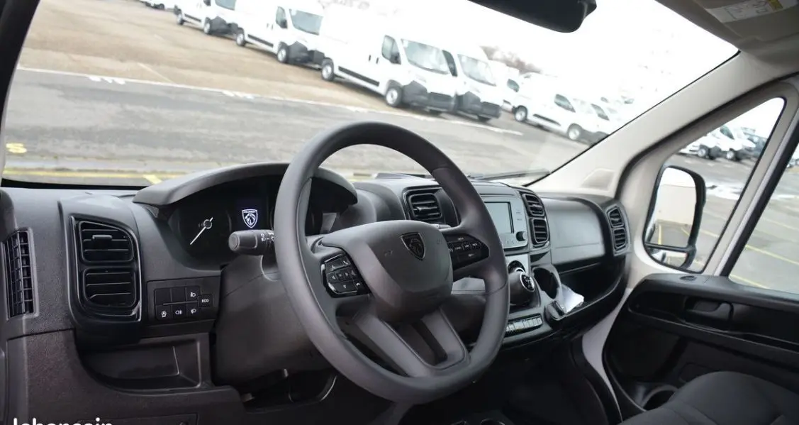 Vue intérieure côté conducteur du Peugeot Boxer Fourgon blanc Icy, volant cuir avec commandes intégrées et tableau de bord moderne.