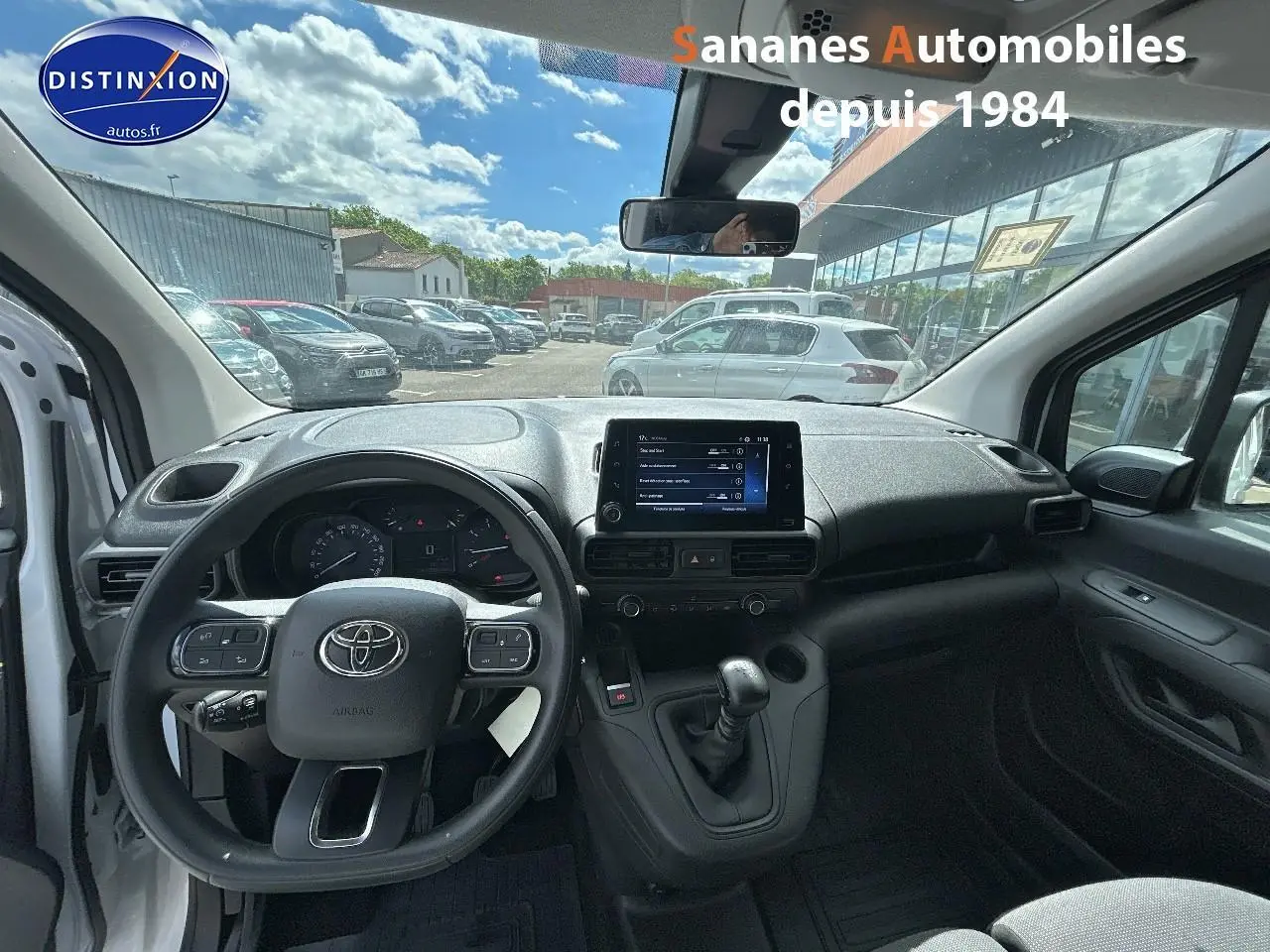 Vue intérieure avant du Toyota Proace City 2023 blanc, montrant le volant, la console centrale avec écran tactile et la boîte manuelle.