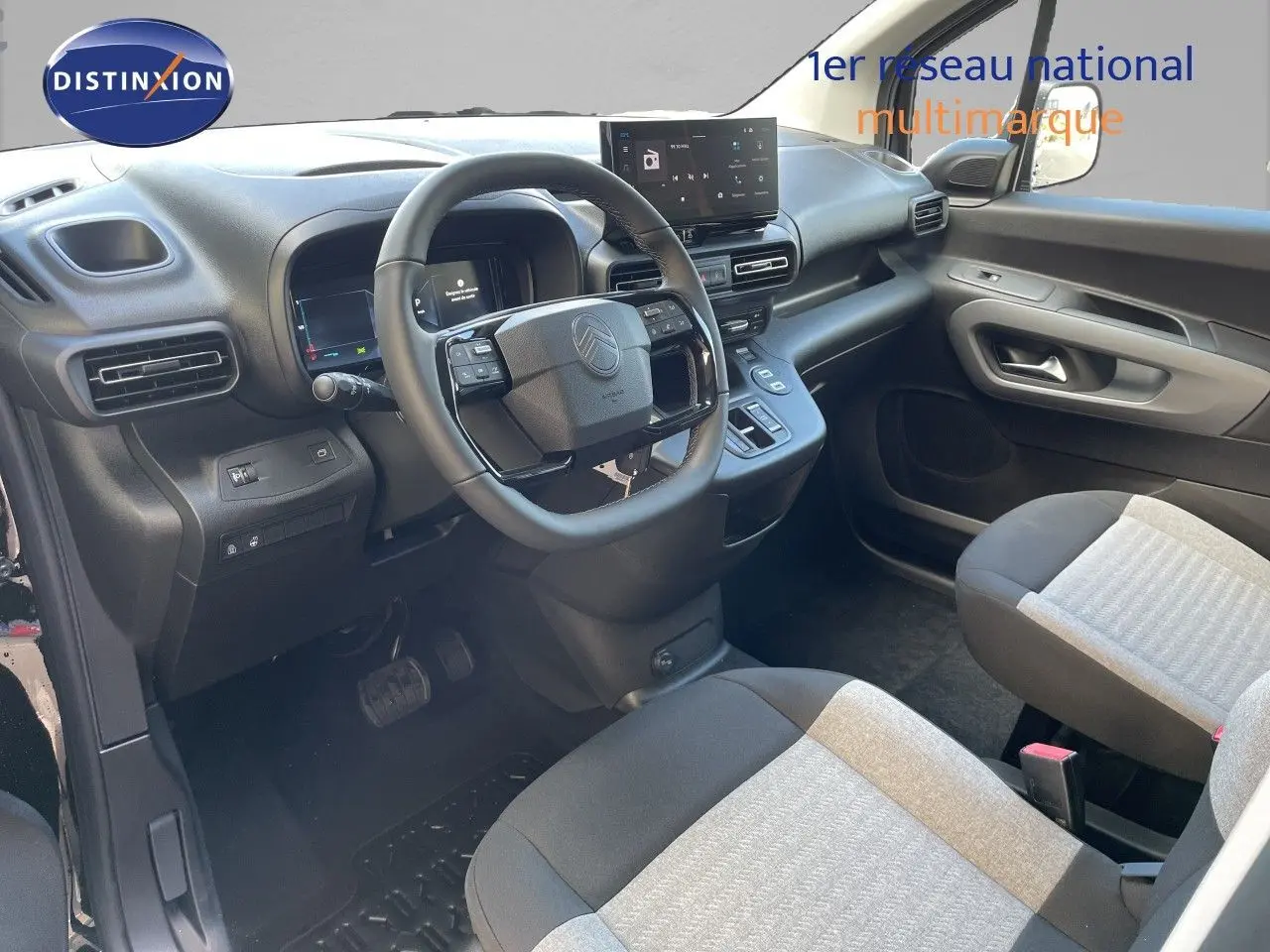Vue intérieure côté conducteur du Citroën Berlingo 2026, tableau de bord noir avec écran tactile et sièges tissu bicolore.