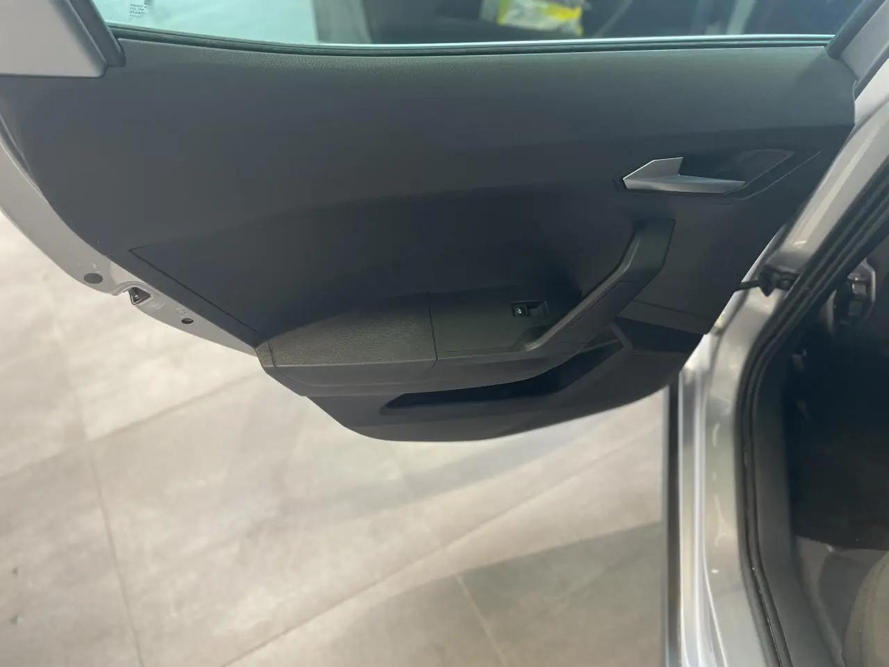 Vue intérieure de la porte avant droite d'une SEAT Arona 2024 gris clair avec poignée argentée et commande de vitre.