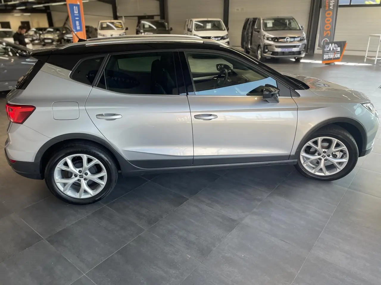 Vue latérale droite d'un SEAT Arona 2024 gris GRS avec toit noir et jantes alliage 16 pouces en showroom.