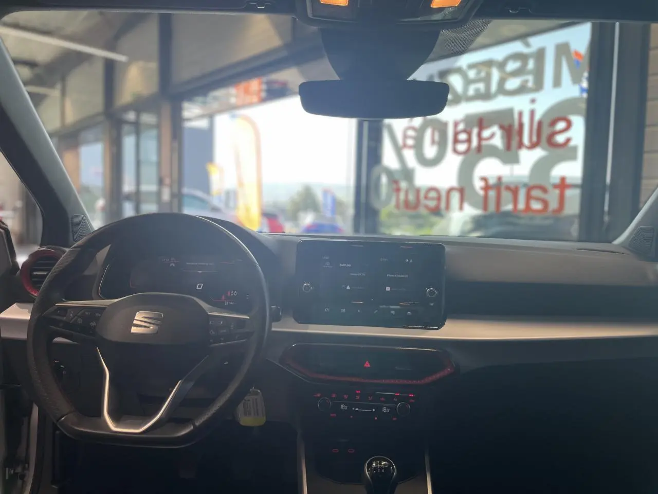Vue intérieure avant du SEAT Arona 2024 rouge Passion, avec volant sport cuir, écran tactile et détails rouges sur la console.