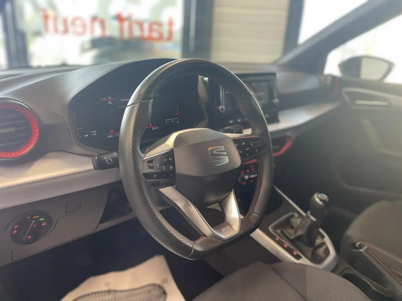 Vue intérieure centrée sur le volant sport cuir avec logo SEAT, tableau de bord digital et levier de vitesse manuel.